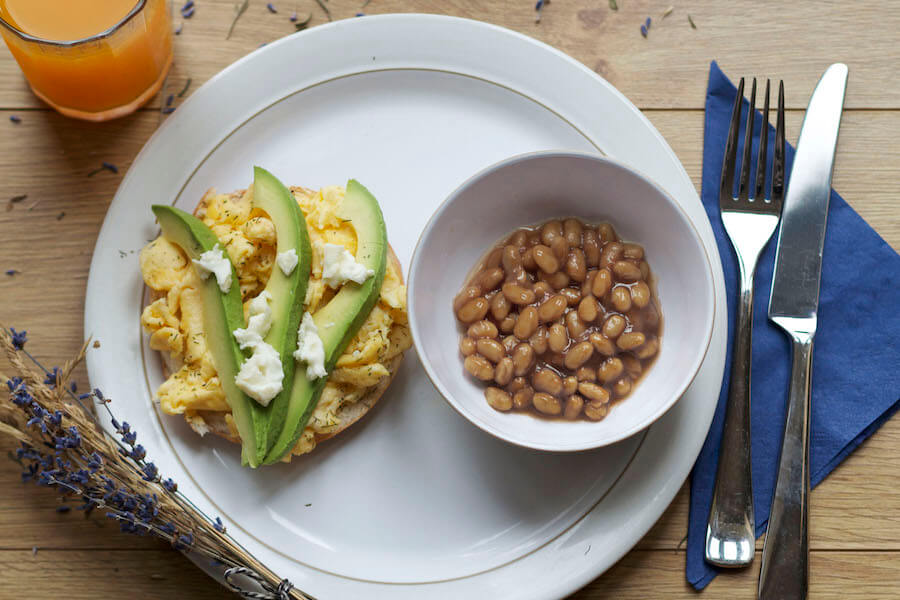 Breakfast with a bagel, eggs, avocado slices, and fresh oven-baked beans