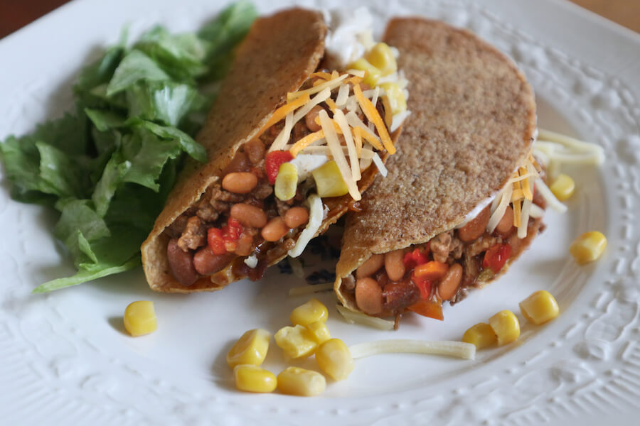 Tacos de blé entier garnis de chili aux légumes L'Héritage, fromage râpé et grains de maïs, servis avec laitue